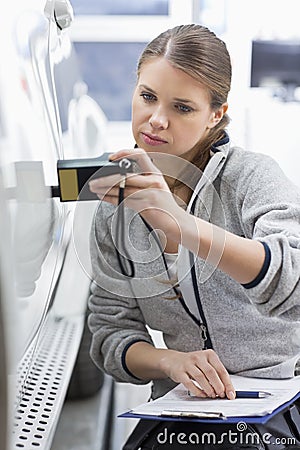 Female maintenance engineer checking car paint with equipment in workshop Stock Photo