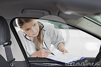 Female maintenance engineer with clipboard examining car's interior in workshop Stock Photo