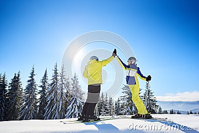 Female and male skiers high five to each other under sunny blue sky. Successful skiing up to mountain top. Full-length. Stock Photo