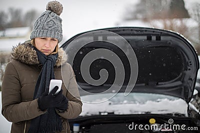 Female Motorist Broken Down In Snow Calling For Roadside Assistance On Mobile Phone Stock Photo