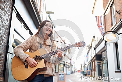 Female Musician Busking Playing Acoustic Guitar Outdoors In Street Stock Photo