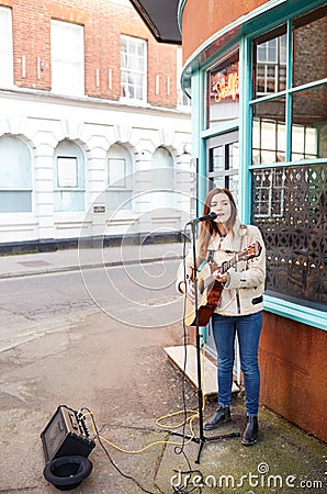Female Musician Busking Playing Acoustic Guitar And Singing Outdoors In Street Stock Photo