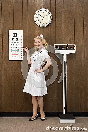 Female nurse pointing to eye chart in retro setting. Stock Photo