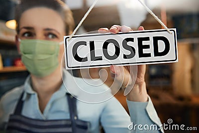 Female Owner Of Small Business Wearing Face Mask Turning Round Closed Sign During Health Pandemic Stock Photo