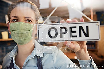 Female Owner Of Small Business Wearing Face Mask Turning Round Open Sign During Health Pandemic Stock Photo