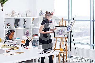 Female painter drawing in art studio using easel. Portrait of a young woman painting with aquarelle paints on white Stock Photo