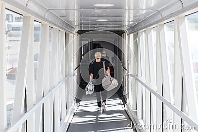 Female passenger carrying the hand luggage bag, walking the airplane boarding corridor. Stock Photo