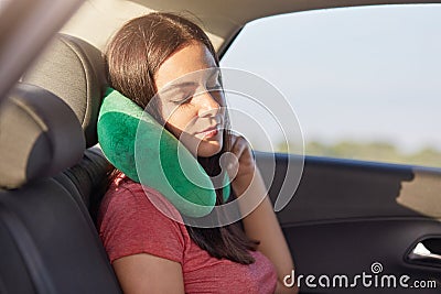 Female passenger sleeps in car while rides on long distance, uses small pillow as has pain in neck, takes nap, has rest, feels tir Stock Photo