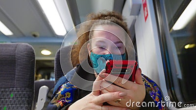 Female passenger wearing face covering mask during covid-19 lockdown using phone inside train in england uk Editorial Stock Photo