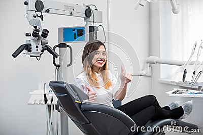 Female patient with perfect white teeth sitting in dental chair, smiling and showing thumbs up after treatment Stock Photo