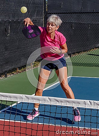 Female pickelball player volleys the ball over the net Stock Photo