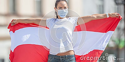 Female in protective mask holds a flag of Austria behind her outdoors on a sunny day Stock Photo