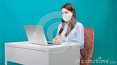 Female in protective mask works on laptop at workplace or at home during a pandemic. The concept of work during Stock Photo