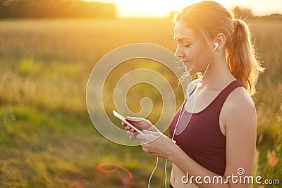 Female runner enjoying calm atmosphere while jogging on field, listening to her favourite track in earphones. Young female going i Stock Photo