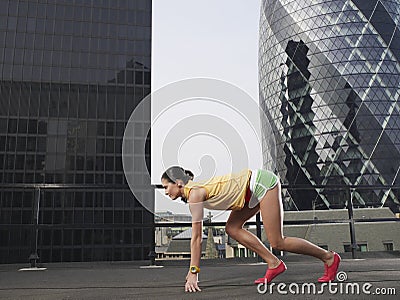 Female Runner In Start Position Against Buildings Stock Photo