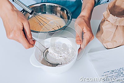 Female`s hands scoop flour in sieve to sift it into the dough Stock Photo