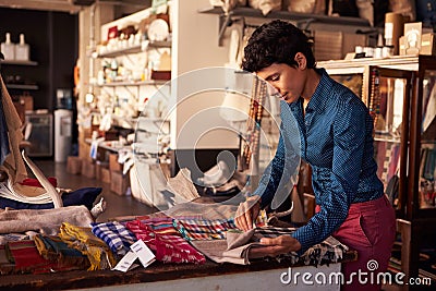 Female Sales Assistant Arranging Textiles In Homeware Store Stock Photo