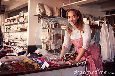 Female Sales Assistant Arranging Textiles In Homeware Store Stock Photo