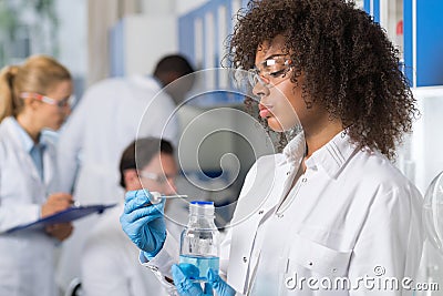 Female Scientific Researcher In Laboratory, African American Woman Working With Flask Over Group Of Scientist Making Stock Photo