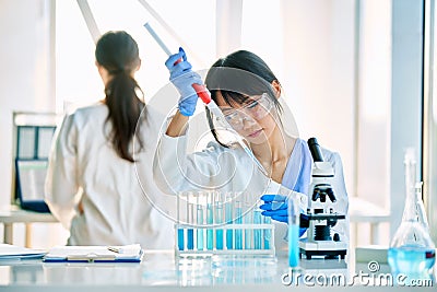 Female scientist making microbiology research using pipette, flask and test tubes working in modern chemical lab Stock Photo