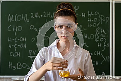 female scientist in white coat and glasses holding laboratory flask with red liquid Stock Photo