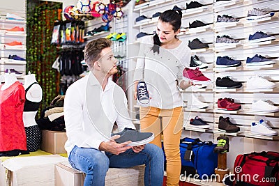 Female seller demonstrating sneakers to customer in sports store Stock Photo