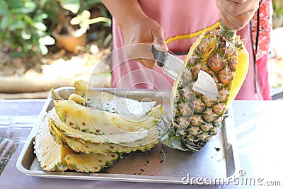 Female seller's hands using a knife to pare pineapple Stock Photo