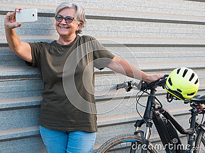 Female senior people active grandmother standing close to his e bike doing a selfie. Healthy lifestyle for retired person. Yellow Stock Photo