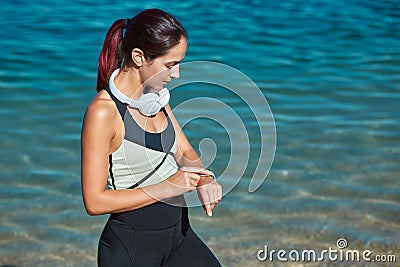 Female sets timer for workout. Lady in sportswear and headset. Training out on fresh air. Sport time and fitness idea Stock Photo