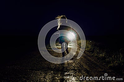 female silhouette on a night country road running away from pursuers by car in the light of headlights Stock Photo