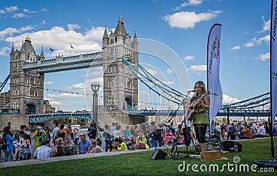 Female singer guitarist performing on south bank with Tower bridge in background in London, UK Editorial Stock Photo