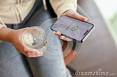 A female sipping water, relaxing in a cafe and using WhatsApp on her phone Editorial Stock Photo