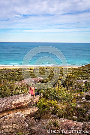 Female sitting on rocks in active wear with views out to beach and ocean Stock Photo