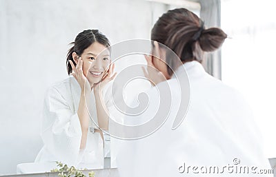 Female Skin Care. Young asian woman touching her face and looking to mirror in bathroom. Stock Photo