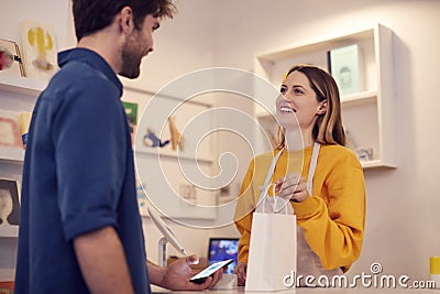 Female Small Business Owner Accepting Contactless Payment In Shop From Customer Using Mobile Phone Stock Photo