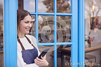 Female Small Business Owner With Digital Tablet Standing In Shop Doorway On Local High Street Stock Photo