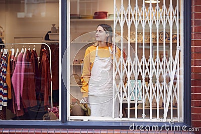 Female Small Business Owner Pushing Back Security Grill And Opening Shop Stock Photo