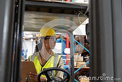 Female staff writing on clipboard while sitting on forklift Stock Photo