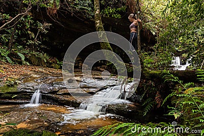 Female standing on tree trunk exploring waterfalls in lush wilderness Stock Photo