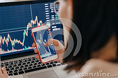 Female stock market investor using laptop and cellphone app for investment at home Stock Photo