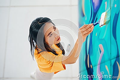 Female street artist painting colorful graffiti with paintbrushe on wall Stock Photo