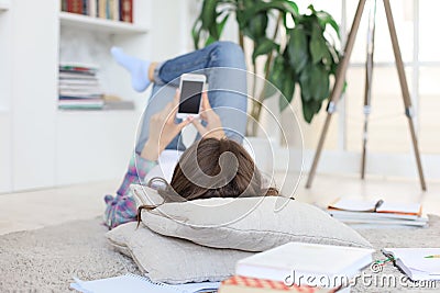 Female student checking social media before getting back to studying, lying on floor against cozy domestic interior Stock Photo