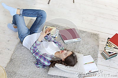 Female student checking social media before getting back to studying, lying on floor against cozy domestic interior Stock Photo