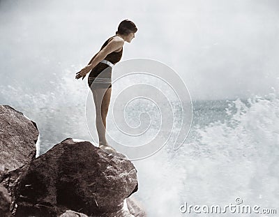 Female swimmer on rock above crashing surf Stock Photo