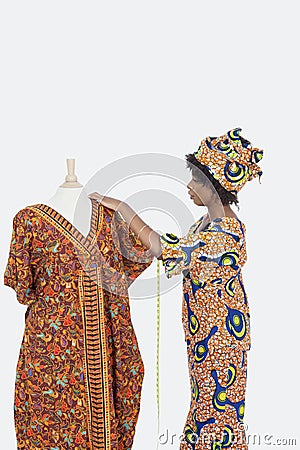 Female tailor in traditional outfit measuring dashiki on tailor's dummy over gray background Stock Photo