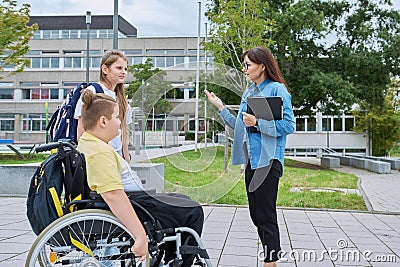 Female teacher and children, boy in wheelchair and girl talking outdoor Stock Photo