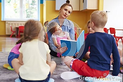 Female teacher and group of children are reading a book Stock Photo