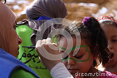 Female teacher painting little girls face in butterfly shape in playground Editorial Stock Photo