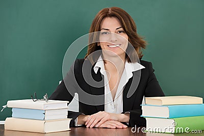 Female Teacher Sitting At Classroom Desk Stock Photo