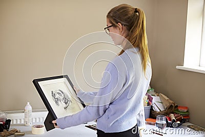 Female Teenage Artist Holding Framed Charcoal Drawing Of Dog In Studio Stock Photo